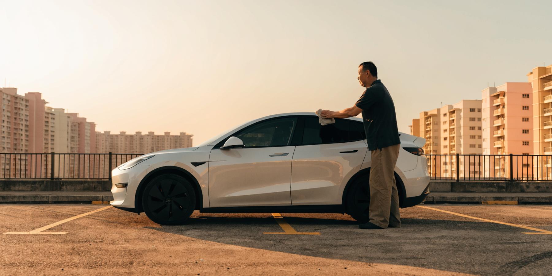 A driver calmly wiping down his modern electric SUV in a quiet HDB carpark at golden hour